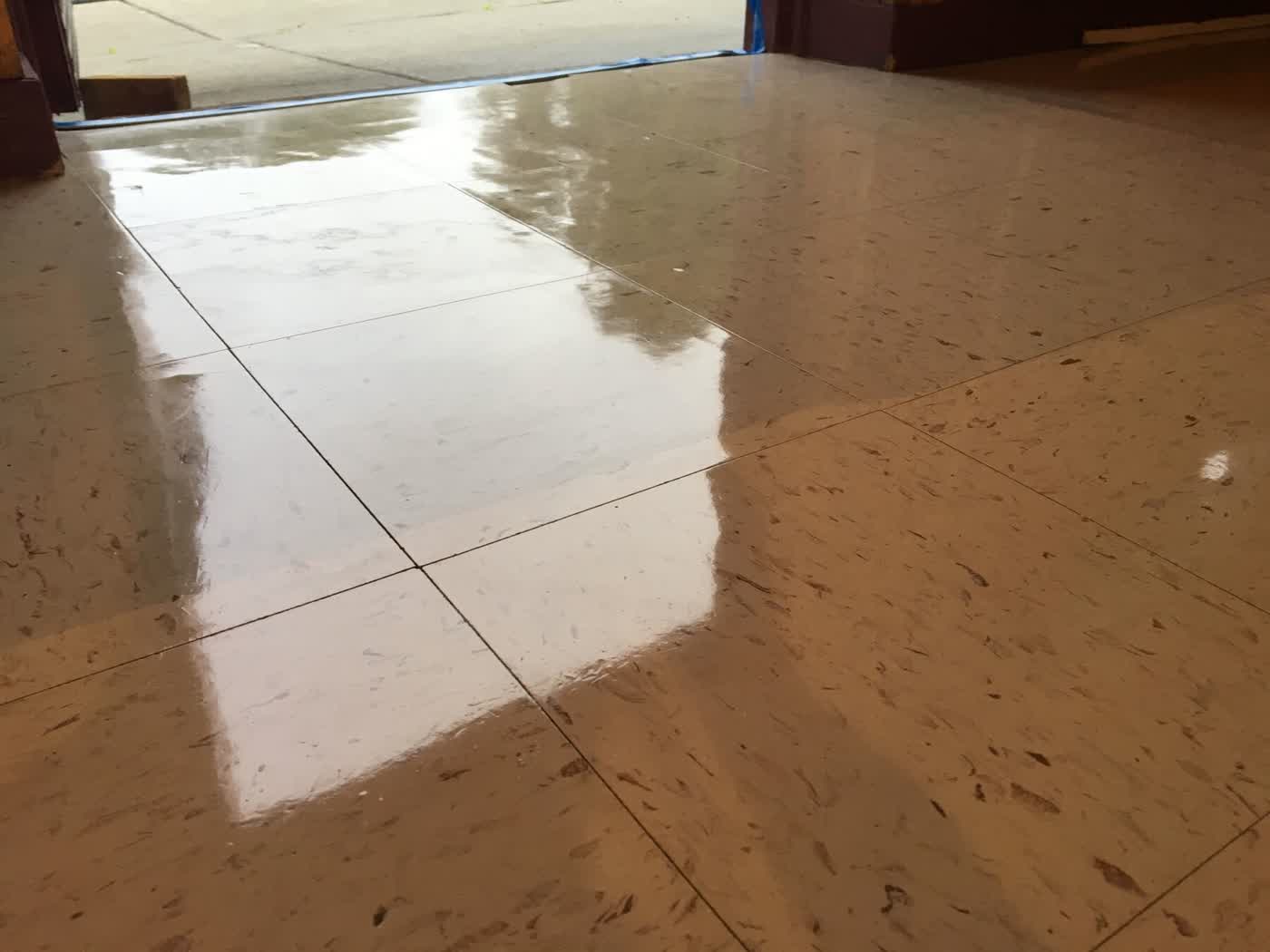 Beige mottled VCT at an exterior door, film reflecting daylight