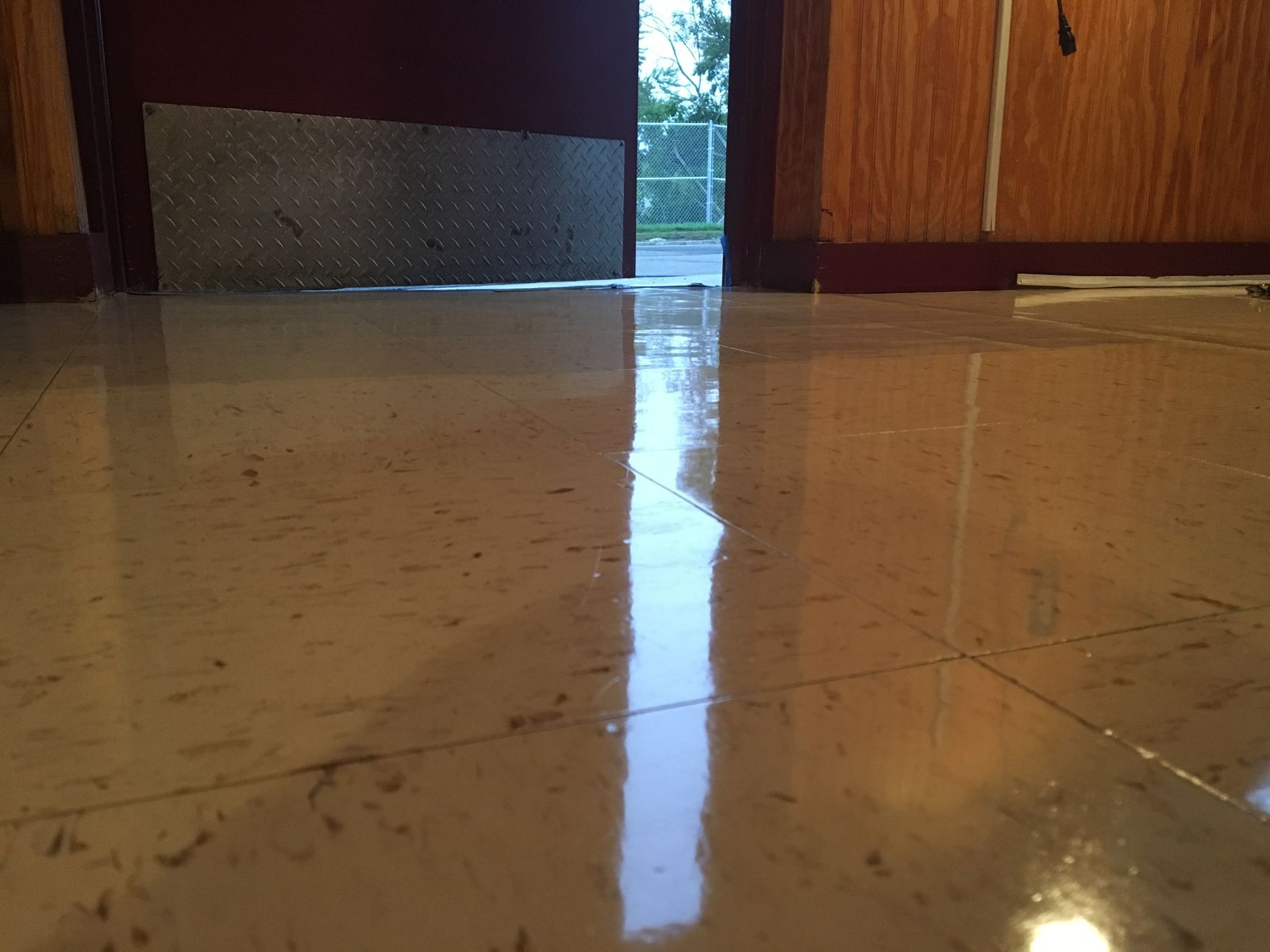 The same doorway and diamond-plate kick plate after work, beige VCT with a high-gloss finish