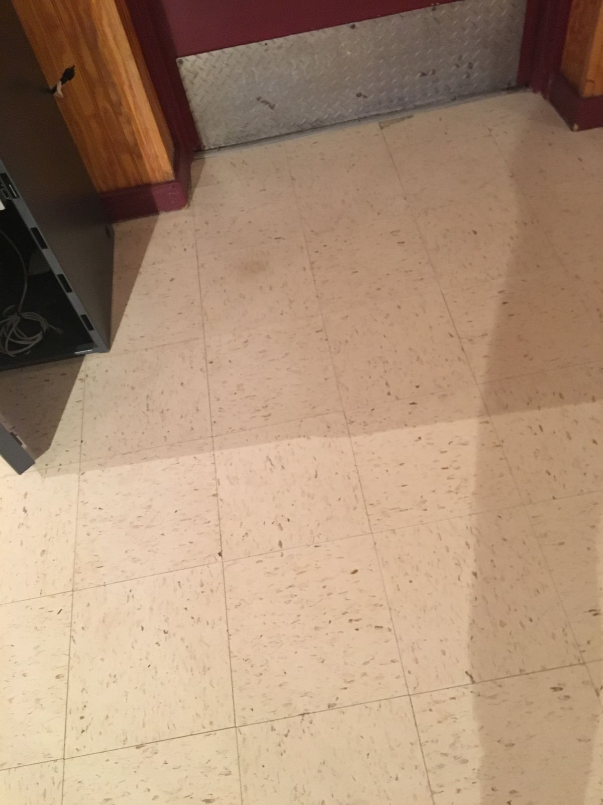 Dull, worn beige VCT at a doorway with a diamond-plate kick plate, before work