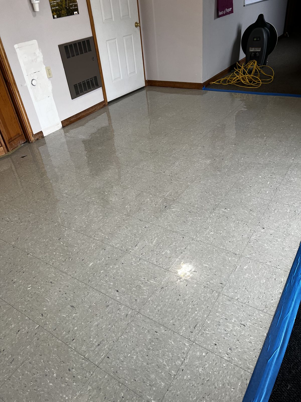 Gray VCT room with an air mover and blue tape while finish dries